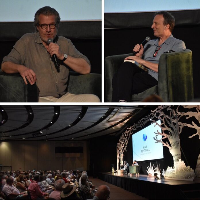 Das Bild zeigt oben rechts den Historiker und Autor Philipp Blom, links den Rektor des IWM, Misha Glenny und unten Philipp Blom, Misha Glenny und das Publikum in einem Auditorium vor einer Leinwand mit dem Titel „Hay Festival“.