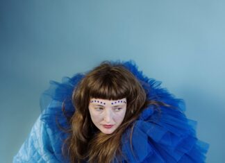 Alicia Edelweiss / Botschaft Lettland Das Bild zeigt Alicia Edelweiss von oben fotografiert vor einem blauen Hintergrund. Sie trägt ein großes Kostüm aus dunkelblauem Tüll.