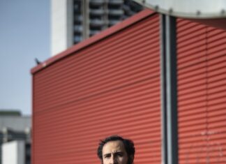 Das Ende ist nah / Kulturforum Bern Das Foto zeigt den Autor Amir Gudarzi stehend vor einer roten Häuserwand.