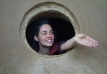 Calliope. Join the Dots / Botschaft Athen Auf dem Bild ist die Architektin und Hebamme Anka Duer zu sehen, sie streckt die Hand aus einer runden Öffnung - vermutlich aus dem auf Lehm gebauten Geburtsraum in unmittelbarer Nähe des Frauenmuseums Hittisau - entgegen.