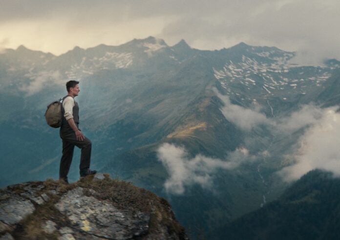 Das Bild zeigt einen Mann, der vor majestätischen Bergen steht und in die Ferne blickt.