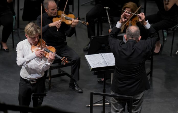 Bild: Juan Pablo Garretón Das Bild zeigt den Geiger Yury Revich während der Interpretation des Paganini Violinkonzertes beim pizzicato und rechts von ihm den Dirigenten des chilenischen Nationalorchesters beim Dirigieren. Dahinter sieht man zwei Streicher aus dem Orchester.