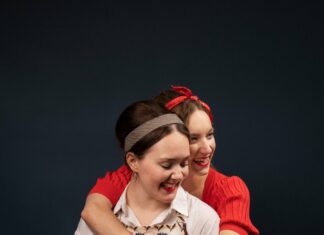 The Good Women / Kulturforum London Das Bild zeigt die beiden Schauspielerinnen Lena Liedl und Faith McCune in ihren Bühnenkostümen. Eine umarmt die andere, indem sie ihre Arme über die Schultern der anderen legt.