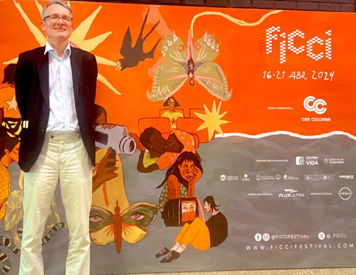 Das Bild zeigt Gesandten Alexander Springer von der ÖB Bogota, hinter ihm eine orangefarbene Plakatwand mit dem Logo des Internationalen Filmfestivals von Cartagena und einigen Illustrationen.