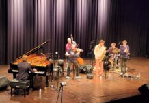 EUNIC JAZZ EXPRESS / Österreichische Botschaft Brasilia Das Bild zeigt eine Bühne mit links einem Klavier und Pianisten, mittig dem Jazzgeiger Rudi Berger im Vordergrund und Kontrabassisten im Hintergrund, sowie rechts daneben einen Saxofonist, Schlagzeuger und Trompeter, alle ins Spiel eines Liedes vertieft