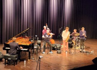 EUNIC JAZZ EXPRESS / Österreichische Botschaft Brasilia Das Bild zeigt eine Bühne mit links einem Klavier und Pianisten, mittig dem Jazzgeiger Rudi Berger im Vordergrund und Kontrabassisten im Hintergrund, sowie rechts daneben einen Saxofonist, Schlagzeuger und Trompeter, alle ins Spiel eines Liedes vertieft