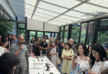 Schmuckkunst zu Gast in der österreichischen Residenz Seoul / Kulturforum Seoul Gäste stehen um eine lange Tafel, auf der zahlreiche Schmuckstücke angeordnet sind; der Schmuckkünstler Benedikt Fischer erläutert seine Werke