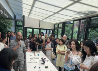 Schmuckkunst zu Gast in der österreichischen Residenz Seoul / Kulturforum Seoul Gäste stehen um eine lange Tafel, auf der zahlreiche Schmuckstücke angeordnet sind; der Schmuckkünstler Benedikt Fischer erläutert seine Werke
