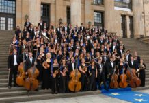 European Union Youth Orchestra/ Kulturforum New York Das Bild zeigt das European Union Youth Orchestra. Die Orchestermitglieder sind alle in schwarz-weiß gekleidet und halten – wo möglich – ihre Instrumente in Händen. Sie tragen zusätzlich einen blauen dünnen Schal