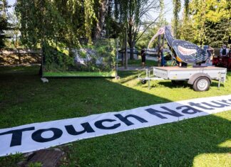TOUCH NATURE / Kulturforum Laibach Das Bild zeigt ein Transparent mit der Aufschrift Touch Nature, eine Fotografie mit einem überwucherten Gewächshaus und die Skulptur eines Waldrapps auf einem Wagen.