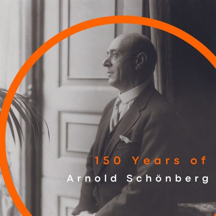 Das Bild zeigt Arnold Schönberg, der am Fenster steht und hinausblickt. Im Bild ist ein oranger Bogen als Designelement sichtbar, unter dem der Schriftzug „150 Years of Arnold Schönberg“ in Orange und Weiß zu sehen ist.