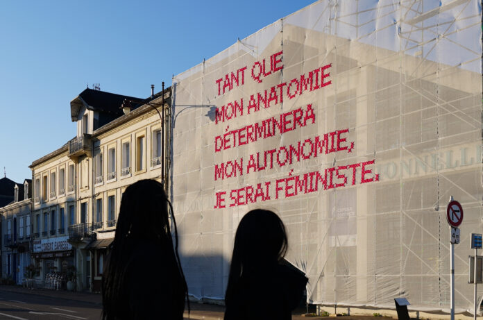 Das Bild zeigt eines der Baunetze von Katharina Cibulka mit der eingestickte Aufschrift „Tant que mon anatomie determineramon autonomie, je serai feministe“