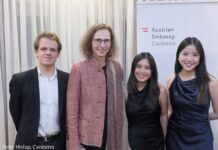 Trio Alpenrose / Botschaft Canberra Das Bild zeigt Botschafterin Kögler mit dem Trio Alpenrose vor einem Logo der Österreichischen Botschaft Canberra