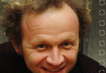 Franz Hautzinger beim FAB_IN FIELD Festival / Kulturforum Warschau Auf dem Bild sieht man einen Mann von den Schultern aufwärts. Der Mann hat lockiges, helles Haar und trägt einen dunklen Pullover, mit einem groben Muster. Er lacht freundlich in die Kamera.