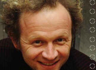 Franz Hautzinger beim FAB_IN FIELD Festival / Kulturforum Warschau Auf dem Bild sieht man einen Mann von den Schultern aufwärts. Der Mann hat lockiges, helles Haar und trägt einen dunklen Pullover, mit einem groben Muster. Er lacht freundlich in die Kamera.