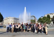 Treffen der Österreich-Bibliotheken des Außenministeriums Das Bild zeigt ein Gruppenfoto der Seminarteilnehmerinnen und -teilnehmer vor dem Brunnen am Schwarzenbergplatz dessen Fontäne von einen Regenbogen erleuchtet wird