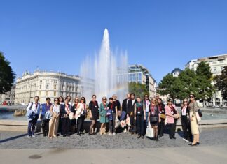 Treffen der Österreich-Bibliotheken des Außenministeriums Das Bild zeigt ein Gruppenfoto der Seminarteilnehmerinnen und -teilnehmer vor dem Brunnen am Schwarzenbergplatz dessen Fontäne von einen Regenbogen erleuchtet wird