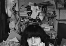 Ich bin so FLEUR dasz nichts mehr geht / Kulturforum Berlin Das Bild zeigt die österreichische Schriftstellerin Friederike Mayröcker mit schulterlangem, dunklem, Haar und einem ernsten Gesichtsausdruck. Sie stützt ihren Kopf nachdenklich mit einer Hand und schaut direkt in die Kamera. Die Aufnahme ist in Schwarz-Weiß gehalten, wodurch die Gesichtszüge und die Struktur ihres Pullovers besonders betont werden. Die Hintergrunddetails sind unscharf und dezent, sodass der Fokus ganz auf ihrem Gesicht liegt.