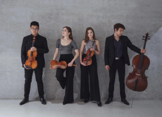 Danube Sounds / Kulturforum Berlin Das Bild zeigt vier Musiker, zwei Frauen und zwei Männer, mit ihren Instrumenten vor einer schlichten, grauen Wand. Von links nach rechts halten die vier Personen zwei Violinen, eine Viola und ein Violoncello. Alle tragen formelle, dunkle Kleidung, die insgesamt elegant und minimalistisch wirkt. Jede Person nimmt im Bild eine individuelle Pose ein, stets in Verbindung mit dem jeweiligen Instrument.