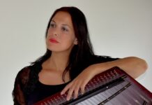 Konzert im Rahmen der Kampagne “Orange the World” / Kulturforum Bratislava Das Bild zeigt ein Foto der Hackbrettistin Hemma Pleschberger-Schmölzer. Sie hält das Hackbrett vor sich in Händen und blickt nach rechts aus dem Bild hinaus mit einem sehnsuchtsvollen Blick, ihre Lippen leuchten in hellem Rot und sie hat lange braune Haare.