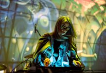 PLASTICPHONIA – Music out of Plastic Trash / Kulturforum Kairo Das Bild zeigt CRYSTN HUNT bei einem Liveauftritt. Sie ist über das Mischpult gebeugt, und hat einen schillernden Stoffumhang, sie ist von gelbblauen Licht angestrahlt