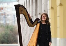 Weihnachtskonzert mit Monika Stadler/ Kulturforum London Das Bild zeigt Monika Stadler in Ganzaufnahme, wie sie leicht an ihre Harfe lehnt und freundlich in die Kamera lächelt.