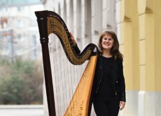 Weihnachtskonzert mit Monika Stadler/ Kulturforum London Das Bild zeigt Monika Stadler in Ganzaufnahme, wie sie leicht an ihre Harfe lehnt und freundlich in die Kamera lächelt.