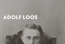 Adolf Loos Ausstellung in Uruguay / Botschaft Buenos Aires Das Bild zeigt das Ausstellungsplakat, auf welchem ein Porträt des Architekten Adolf Loos zu sehen ist. Er sitzt auf einem hohen Lehnstuhl, hat einen Anzug und Krawatte an, die Hände auf dem Schoss ineinander verschränkt und starrt streng in die Kamera. Er ist auf diesem Bild noch jung.