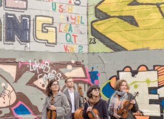 Chaos String Quartet / Kulturforum Ottawa Das Bild zeigt das Chaos String Quartet im Vordergrund, jedes Mitglied mit seinem Instrument in der Hand. Im Hintergrund erstreckt sich eine mit Graffiti bedeckte Wand. Die Mitglieder des Quartetts blicken gemeinsam in dieselbe Richtung – nach rechts.