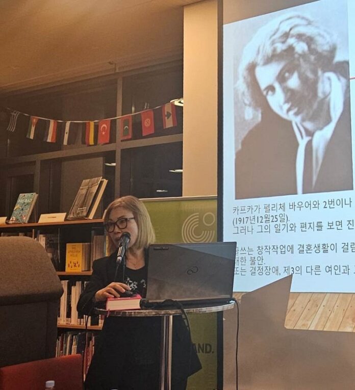 Das Bild zeigt Professor Dr. Jang Eun-soo von der Hankuk University of Foreign Studies (HUFS) beim wissenschaftlichen Einführungsvortrag im Goethe Institut Korea. Sie steht vor einer Bücherwand und einem projizierten Bild von Kafkas Lebensgefährtin Dora Diamant