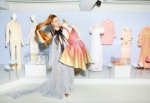 The Future of Living / Kulturforum Brüssel Das Bild zeigt die Designerin Flora Miranda, die stolz einige ihrer Kreationen (hauptsächlich Kleider) vorführt, während sie ihr Haar zurückwirft.