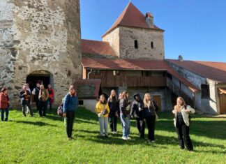 Siebenbürgen Connect / Kulturforum Bukarest Das Bild zeigt die Schülerinnen undSchüler aus Bad Ischl auf einer Reise in Siebenbürgen, Rumänien. Sie stehen vor mittelalterlichen Gebäuden auf einer Wiese, mit blauen Himmel und Sonnenschein.