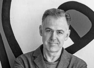 „Circularchitecture – Regeneratives Bauen“ / Kulturplattform Arabischer Raum Das Schwarz-Weiß-Bild zeigt den Vortragenden Thomas Romm, der vor einer Wand mit gekreuzten Armen steht.