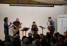 Konzert „Spectrum Saxophonquartett“ / Kulturforum Bratislava Das Bild zeigt das lächelnde „Spectrum Saxophonquartett“ vor einer weißen Wand. Alle sind dunkel angezogen und halten ihre Instrumente.