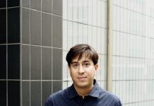 Jaipur-Literaturfestival / Kulturforum New Delhi Das Bild zeigt den Autor Tonio Schachinger, wie er vor einem Gebäude steht. Seine Hände stecken in seinen Hosentaschen und er trägt eine weiße Jeans mit einem dunkelblauen kurzärmligen Hemd.