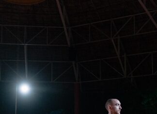 „Insomnia“ / Botschaft Bangkok Das Bild zeigt die Performance „Insomnia“ von Hugo Le Brigand und Alix Eynaudi. Es ist Nacht und ein sehr heller Scheinwerfer beleuchtet Le Brigand, der einen roten kurzärmligen Anzug trägt, und Eynaudi, die ein goldenes Kleid trägt