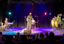 Konzert „Austro-Tunisian Confluence“ / Botschaft Tunis Das Bild zeigt vier Musiker auf einer Bühne, die mit Scheinwerfern in verschiedensten Farben beleuchtet werden. Der Pianist sitzt auf der linken Seite der Bühne, während der Schlagzeuger zentral hinter dem Saxofonisten Niklaus Holler platziert ist. Am rechten Rand der Bühne steht der Perkussionist, umgeben von diversen Instrumenten.