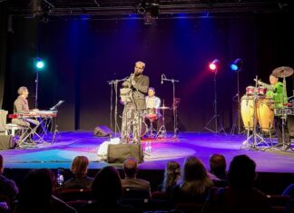 Konzert „Austro-Tunisian Confluence“ / Botschaft Tunis Das Bild zeigt vier Musiker auf einer Bühne, die mit Scheinwerfern in verschiedensten Farben beleuchtet werden. Der Pianist sitzt auf der linken Seite der Bühne, während der Schlagzeuger zentral hinter dem Saxofonisten Niklaus Holler platziert ist. Am rechten Rand der Bühne steht der Perkussionist, umgeben von diversen Instrumenten.