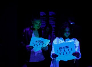 Imagine Dignity /Kulturforum Belgrad Das Bild zeigt zwei Frauen im Dunkeln, die auf ein fluoreszierendes Schild schauen, auf dem Coral Reef steht.