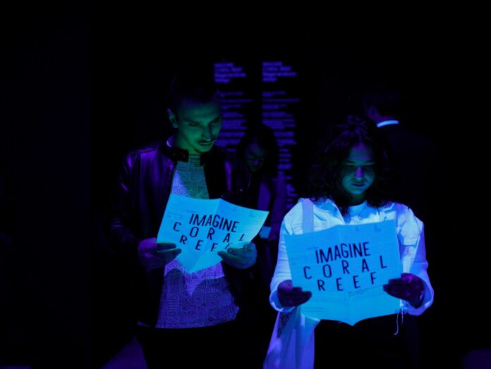 Das Bild zeigt zwei Frauen im Dunkeln, die auf ein fluoreszierendes Schild schauen, auf dem Coral Reef steht.