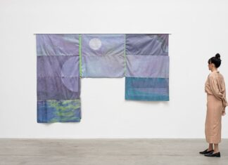 Exhibition: TECHNOFLOWS / Kulturforum New York Das Bild zeigt die Künstlerin Luiza Crosman vor ihrem Kunstwerk aus dem Jahr 208 mit dem Titel COLAPSAR (Dark Matter). Sie steht mit dem Rücken zur Kamera und betrachtet ihr Werk. Das Werk besteht aus lila gefärbten, zusammengenähten Stoffteilen. Auf diesem Kunstwerk sind mehrere kreisförmige Linien zu sehen.