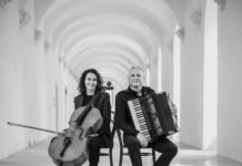 VISION FOR TWO / Kulturforum Rom Das Bild zeigt das Duo sitzend, mit den jeweiligen Instrumenten in der Hand. Links sitzt die Cellistin Asja Valcic und hält ihr Cello, an ihrer rechten Seite ist der Akkordeonist Klaus Paier mit seinem Akkordeon abgebildet