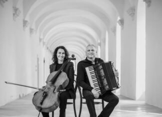 VISION FOR TWO / Kulturforum Rom Das Bild zeigt das Duo sitzend, mit den jeweiligen Instrumenten in der Hand. Links sitzt die Cellistin Asja Valcic und hält ihr Cello, an ihrer rechten Seite ist der Akkordeonist Klaus Paier mit seinem Akkordeon abgebildet