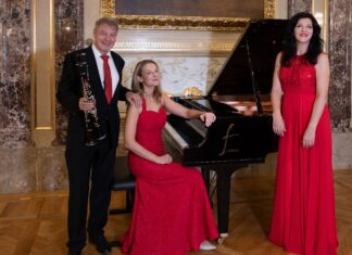 Frauentöne / Kulturforum Sofia Das Bild zeigt das Trio vor einem Klavier. Die Pianistin und die Sopranistin in rotem Kleid. Der Musiker in schwarzem Anzug.