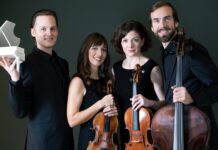 Wiener Klavierquartett / Kulturforum Prag Das Bild zeigt vier Mitglieder des Quartetts stehend und in die Kamera blickend mit ihren Streichinstrumenten und den Pianisten mit einem kleinem Klaviermodells in der Hand.