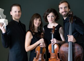 Wiener Klavierquartett / Kulturforum Prag Das Bild zeigt vier Mitglieder des Quartetts stehend und in die Kamera blickend mit ihren Streichinstrumenten und den Pianisten mit einem kleinem Klaviermodells in der Hand.