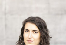 Christina König / Botschaft Oslo Das Bild zeigt die Autorin Christina König vor grauem Hintergrund. Sie trägt einen schwarzen Pullover, darüber eine offene schwarze Lederjacke. Sie schaut leicht seitlich in die Kamera, hat dunkle Augen und ihr dunkelbraunes Haar trägt sie schulterlang geschnitten und mit Seitenscheitel.