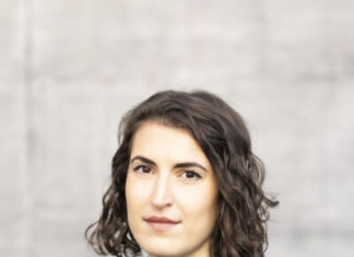 Christina König / Botschaft Oslo Das Bild zeigt die Autorin Christina König vor grauem Hintergrund. Sie trägt einen schwarzen Pullover, darüber eine offene schwarze Lederjacke. Sie schaut leicht seitlich in die Kamera, hat dunkle Augen und ihr dunkelbraunes Haar trägt sie schulterlang geschnitten und mit Seitenscheitel.