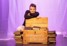 Leb‘ wohl, Bohème / Botschaft Pristina Das Bild zeigt die Schauspielerin Alice Schneider auf der Bühne hinter eine Kiste voller Bücher kniend.