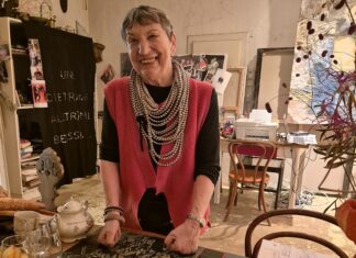 Kunst im Gespräch – Podcastserie Es ist die Künstlerin Linda Waber zu sehen. Sie steht in ihrer Küche und lächelt. vor ihr liegen Orangen.